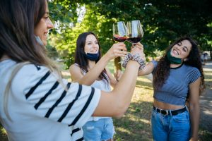 girls toasting with wine glasses wearing face masks 