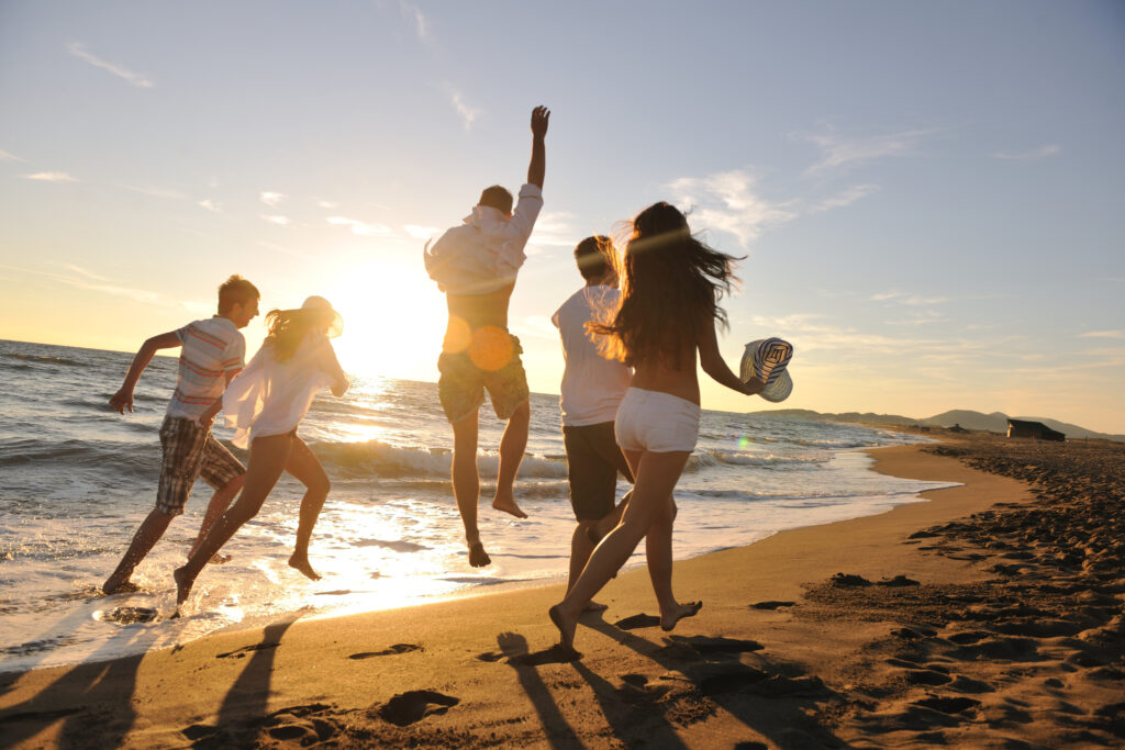happy young people group have fun white running and jumping on beach at sunset time